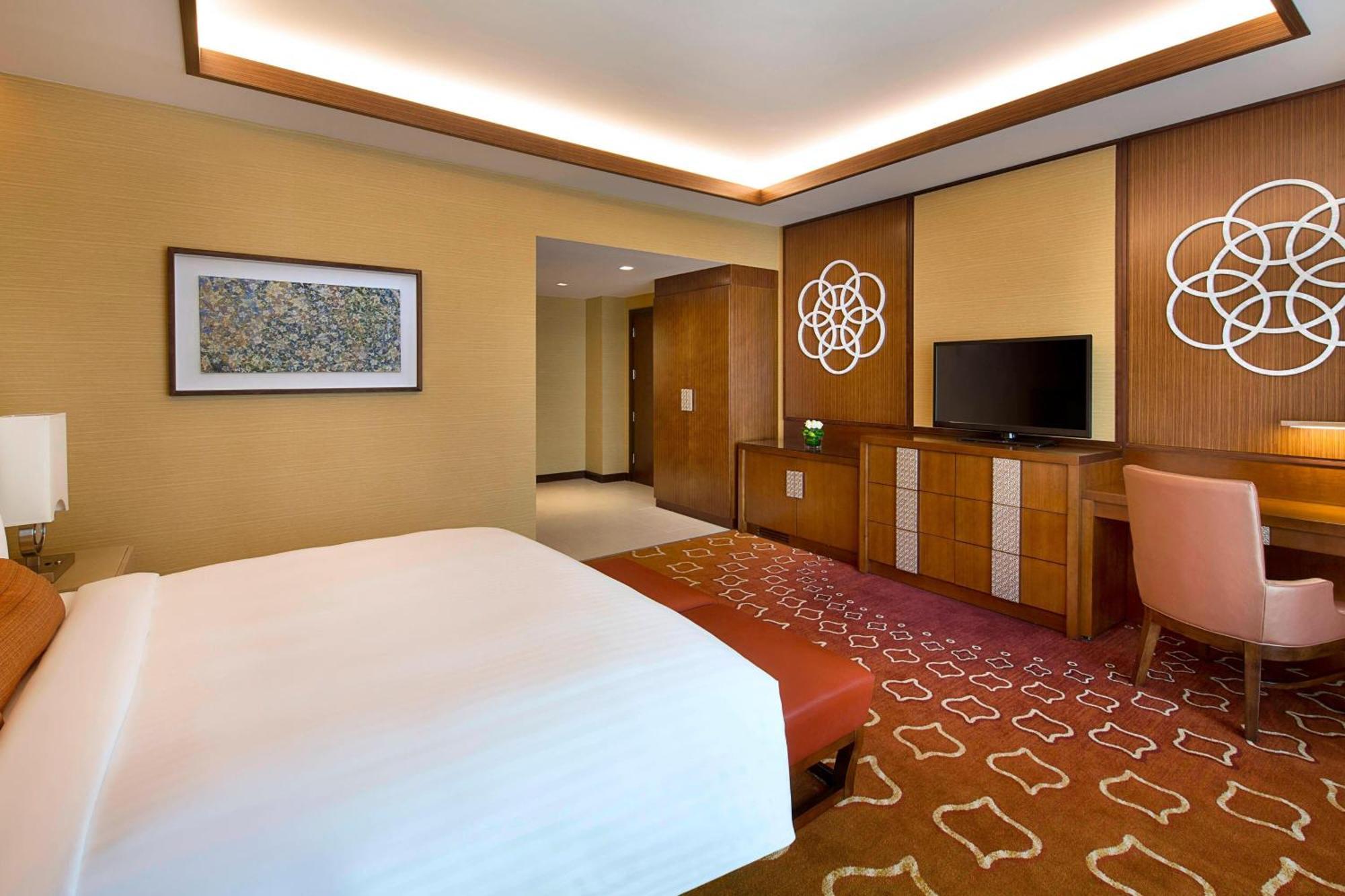 Jabal Omar Marriott Hotel Makkah Mekka Eksteriør billede The photo depicts a modern hotel room featuring a king-sized bed with a white comforter. The room has warm tones, with creamy walls and a patterned carpet in shades of orange. There is a wooden dresser with a flat-screen TV above it. Decorative wall 