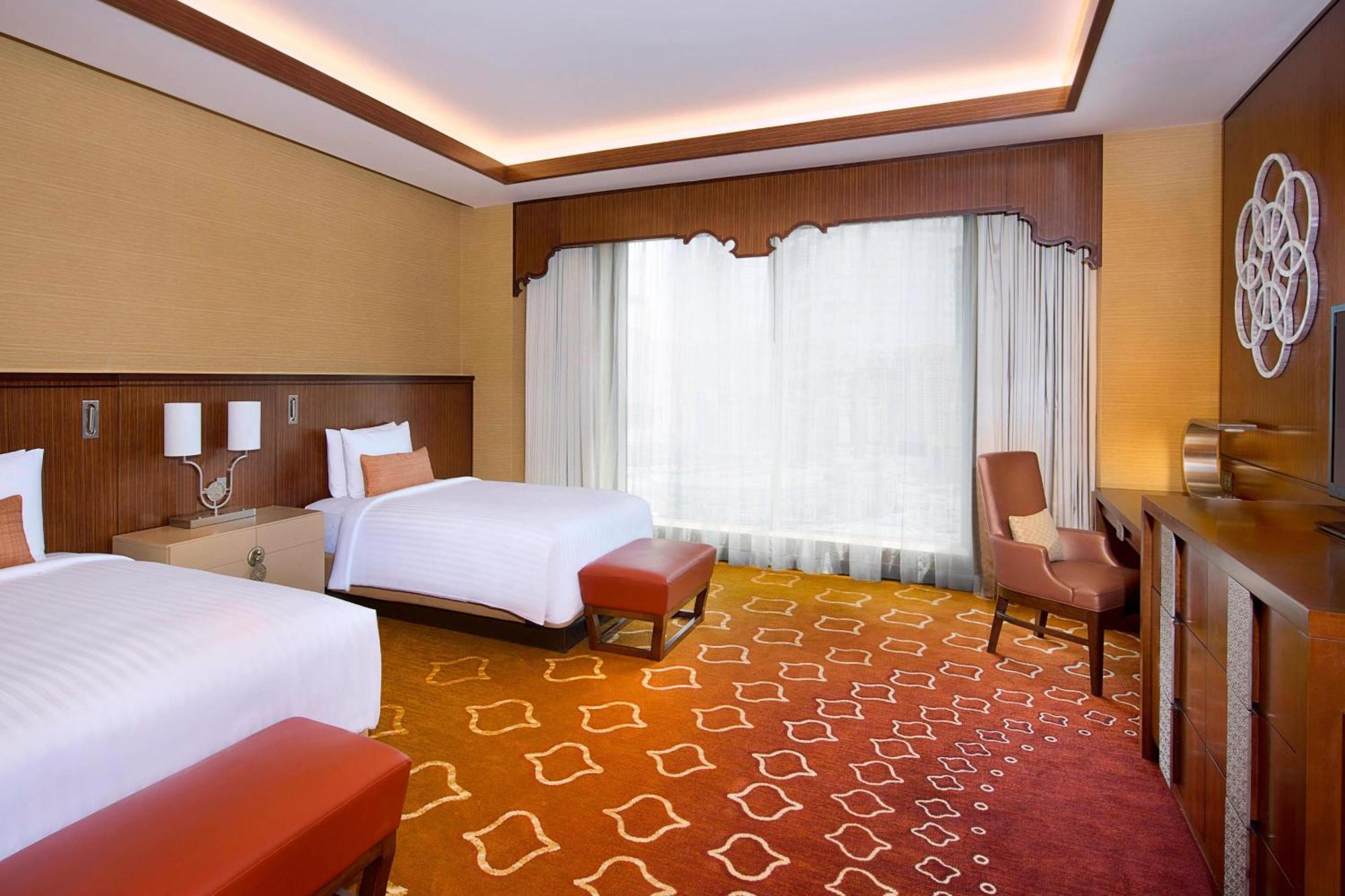 Jabal Omar Marriott Hotel Makkah Mekka Eksteriør billede The photo shows a well-appointed hotel room featuring two beds, one of which is a larger size. The room has a warm color palette with golden and orange tones, accentuated by a stylish carpet that has a geometric pattern. Large windows allow natural l